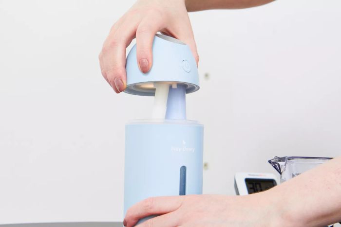 A hand is removing the top of the Hey Dewy Wireless Facial Humidifier