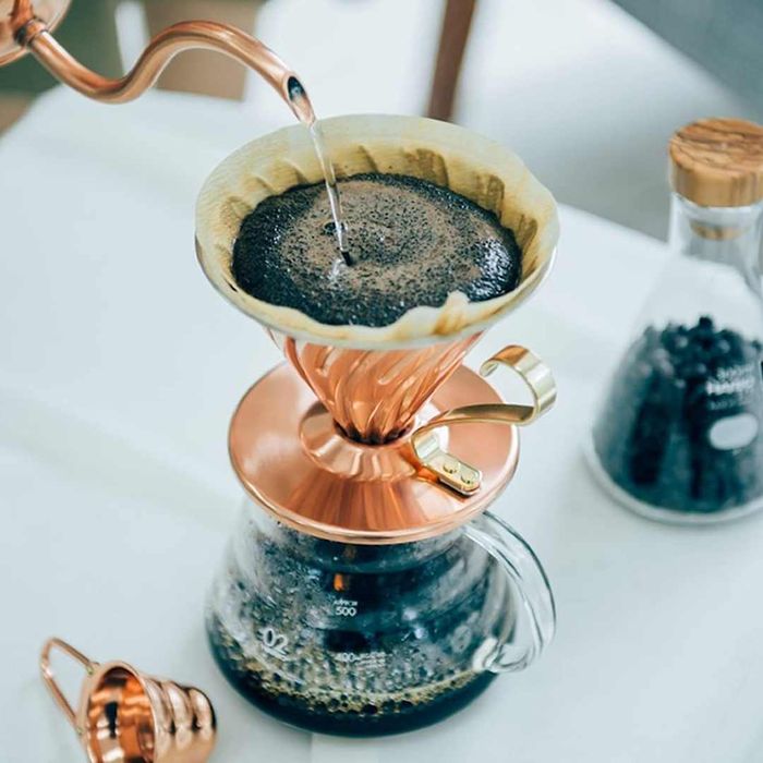 A copper Hario V60 cone dripper perched over freshly brewed coffee.