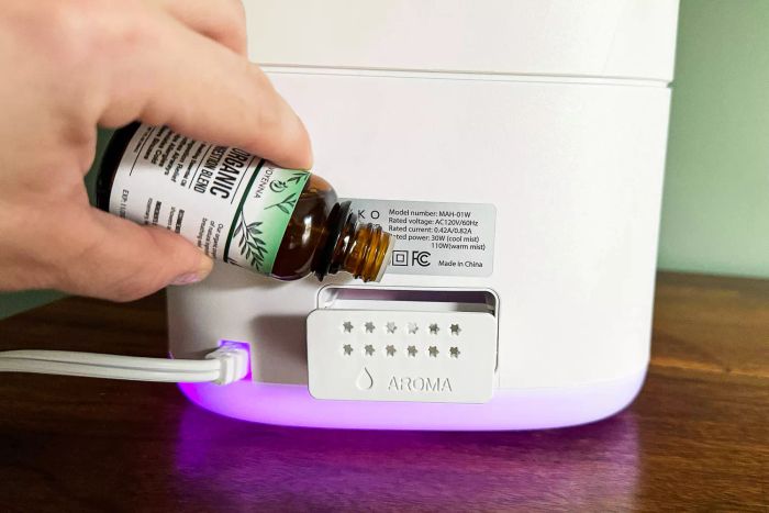 A person is placing essential oil into the aroma diffuser compartment of the Miko Myst Ultrasonic Humidifier