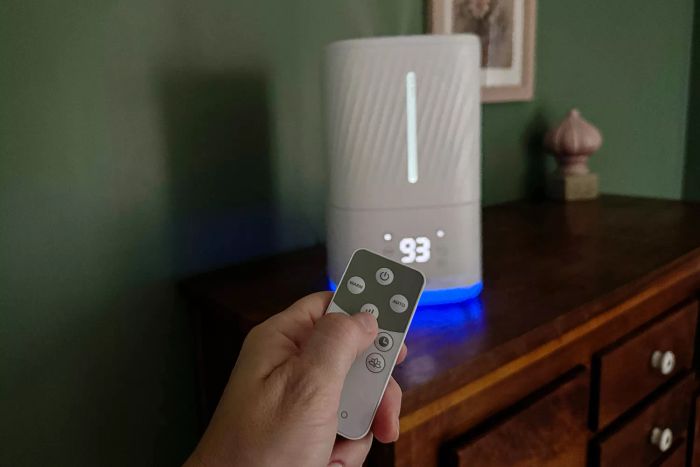 A person is using the remote to modify the settings on the Miko Myst Ultrasonic Humidifier