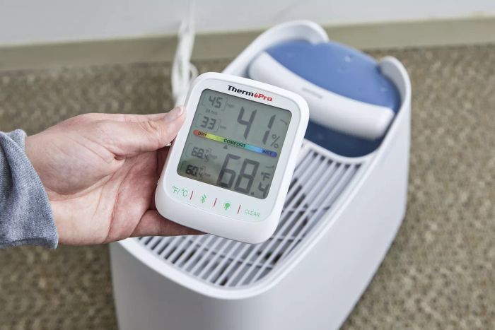 A hand is holding a humidity and temperature meter beside the Honeywell Cool Moisture Humidifier