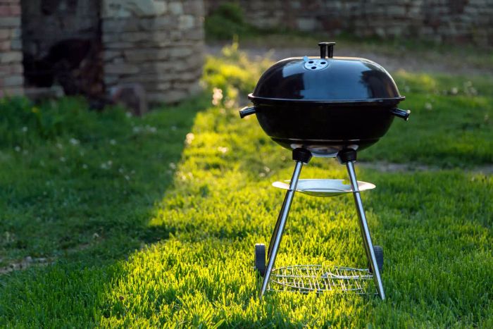 An outdoor BBQ grill placed on the grass, illuminated by sunlight from behind