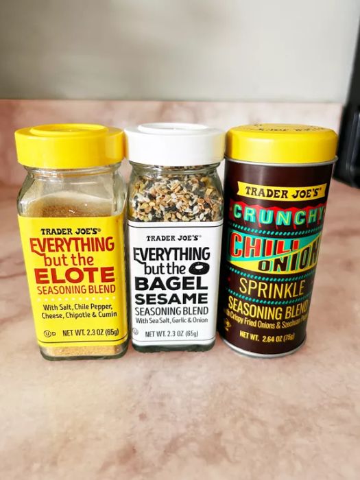 Trader Joe's seasoning blends: Everything but the Elote, Everything but the Bagel, and Crunchy Chili Onion Sprinkle, displayed on a marble countertop.