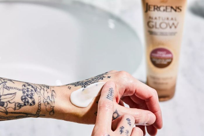 A close-up shot of a person applying the Jergens Natural Glow Firming Moisturizer onto their hand.