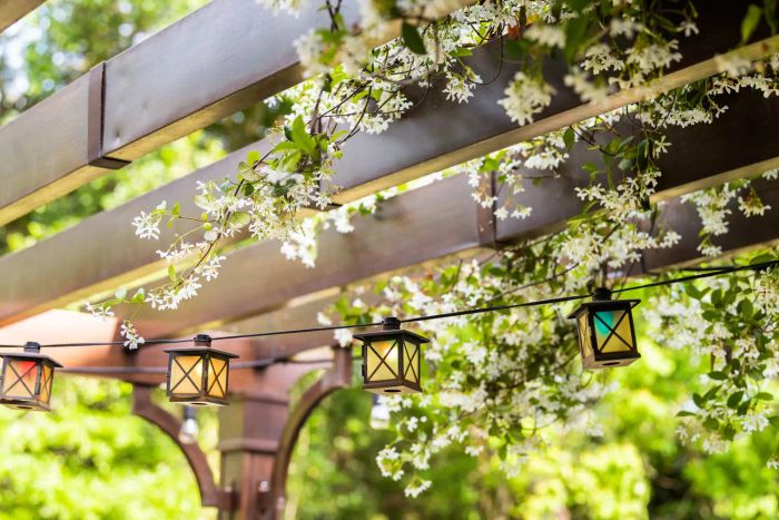 A serene backyard patio with a spring garden, featuring lantern lights hanging from a wooden pergola, surrounded by plants and white flowers