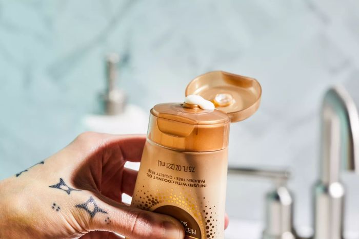 A close-up view of a hand squeezing the Jergens Natural Glow Firming Moisturizer bottle.