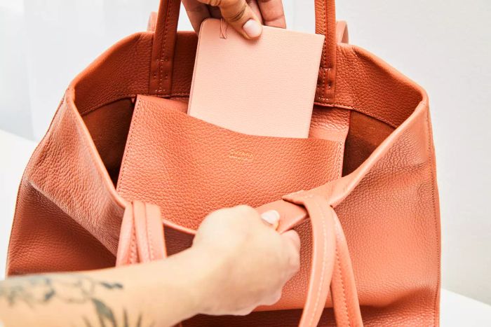 A person retrieves a small notebook from the inner pocket of the Cuyana Tall Easy Tote