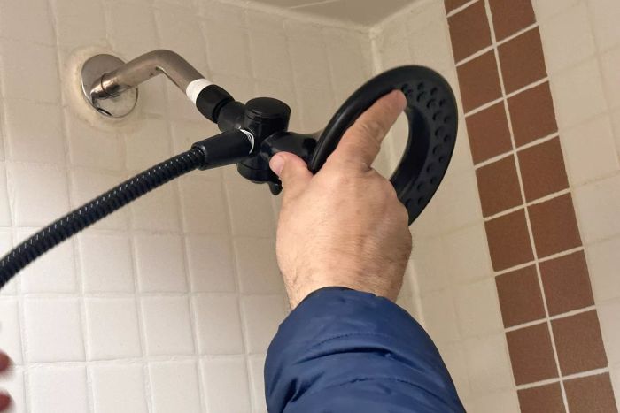 A hand assembling a component of the Delta Faucet 4-Setting In2ition 2-in-1 Dual Shower Head 75486CSN into a shower