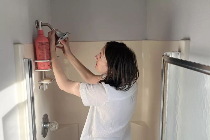 An individual installing the Delta Faucet 52669-BL 5-Setting H2OKinetic Trad Raincan Shower Head