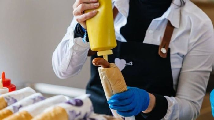 A person adding mustard to a Párek v Rohlíku hot dog.