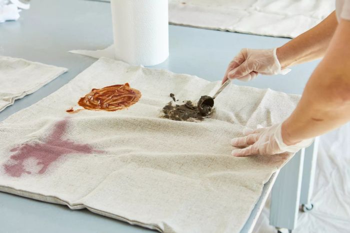 A person applying Rocco & Roxie Supply Co. Oxy Stain Remover to a light-colored fabric to test its effectiveness.