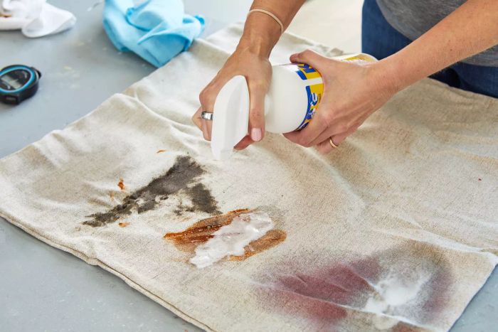 A person applying Kids 'N' Pets Instant Stain and Odor Remover to a pillowcase with a visible stain.