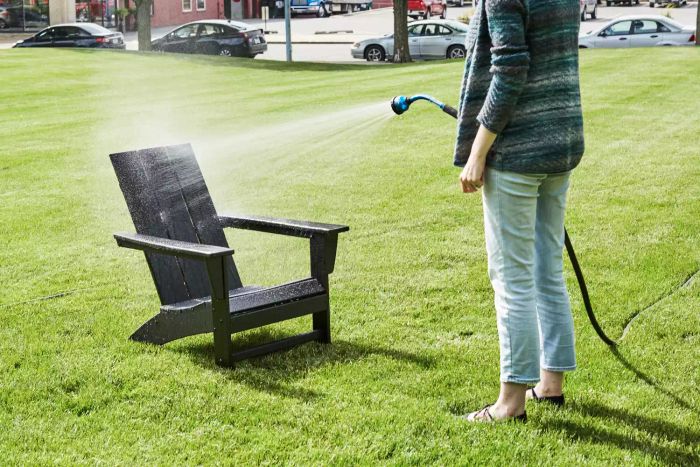 A person using a hose to spray water on the Polywood Modern Adirondack Chair.