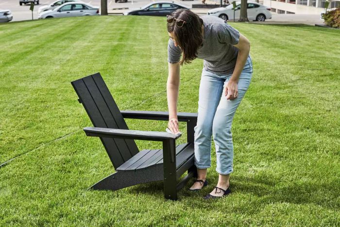 A person cleaning the armrest of the Polywood Modern Adirondack Chair outdoors.