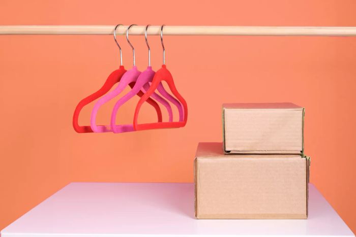 A white table adorned with clothes hangers and paper boxes, alongside a pink dressing room with garments hanging neatly on a rack.