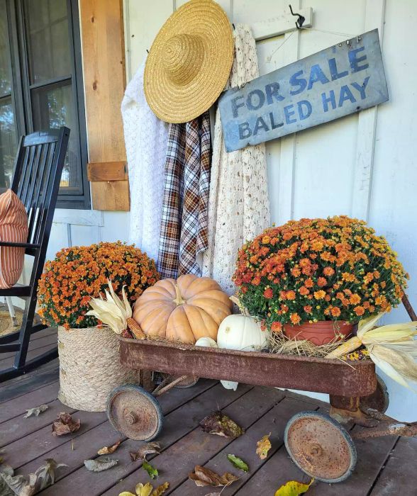 A vintage wagon placed on a front porch, surrounded by autumn decorations.