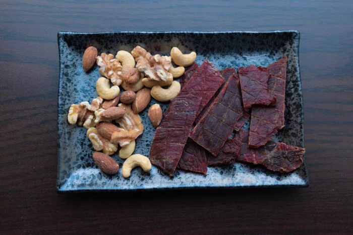 Mixed nuts and dried beef jerky served on a dark-colored tray