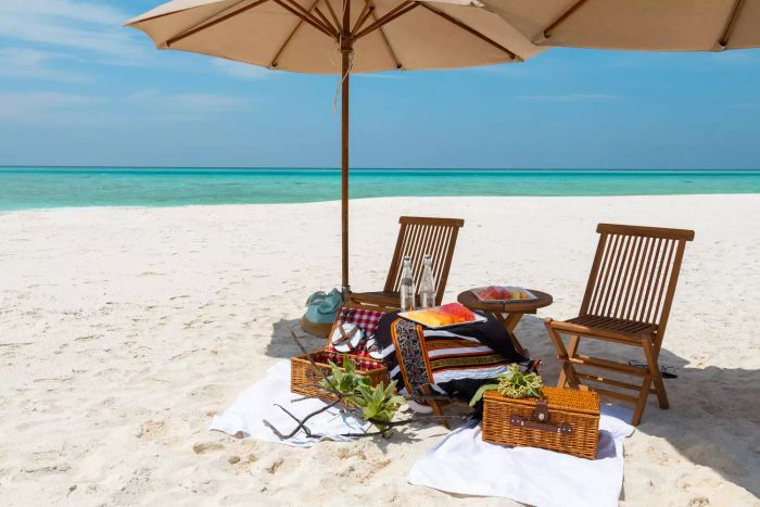 A romantic Maldives beach picnic featuring fresh fruits, parasols, and the stunning turquoise waters of a secluded sandbank