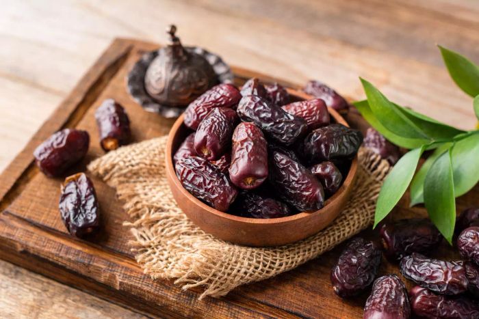 Dried date fruits in a wooden bowl on a wooden tray, on a wooden surface
