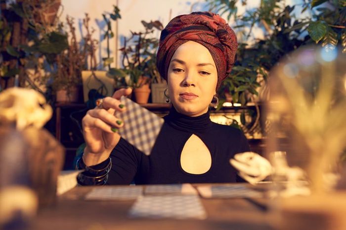 A woman skilled in divination sits at a table, interpreting tarot cards