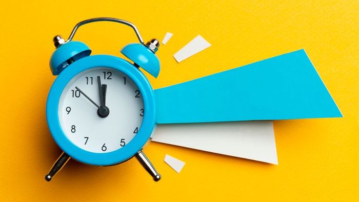 A vibrant blue alarm clock set against a bright yellow backdrop