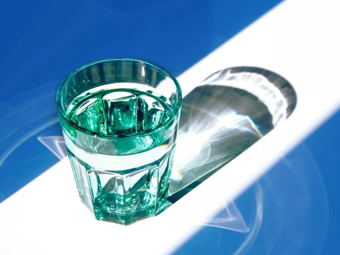 A green glass of water with sunlight, shadows, and reflections.