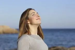 A woman inhales deeply while standing on the beach.