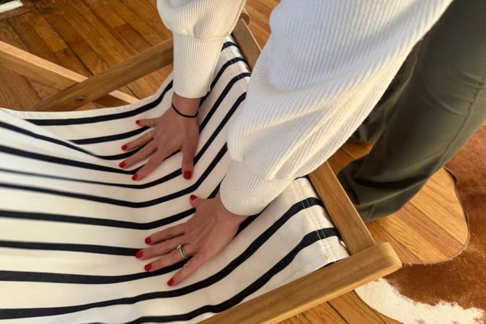 A person adjusting the Serena & Lily Teak Sling Chair