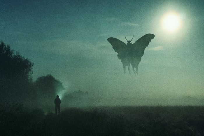 A person holding a flashlight gazes at a massive, moth-shaped figure outlined by the glow of a full moon