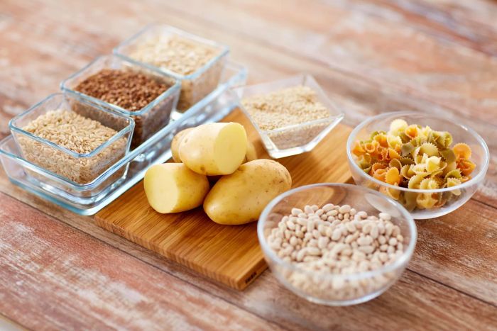A close-up of grain, pasta, and beans in glass bowls alongside potatoes on a table, representing diet, cooking, and carbohydrate-rich foods.
