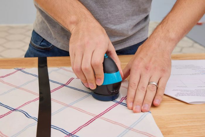 A detailed view of an individual operating the Rowenta Portable Lint Remover Shaver with Adjustable Shave Height on a fabric surface.