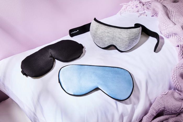 A trio of sleep masks resting on a pillow next to a lavender-colored blanket.