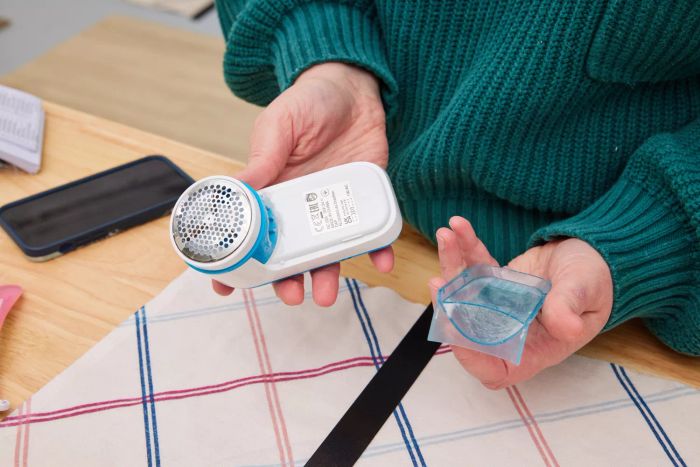 An individual holding the Philips GC026 Electric Lint Remover and Fabric Shaver in one hand and a transparent compartment in the other.