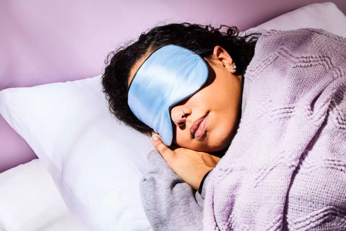 A woman comfortably wearing the Tim & Tina Sleep Mask as she prepares for bed.