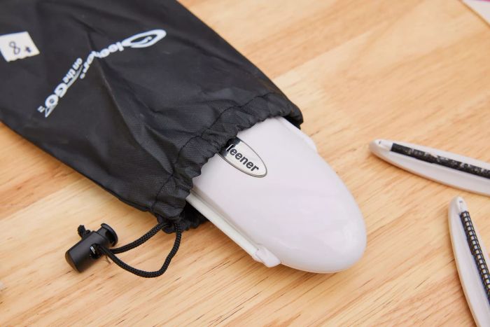The Gleener On The Go Portable Compact Fabric Shaver & Lint Remover placed on a wooden floor alongside its storage bag and accessories