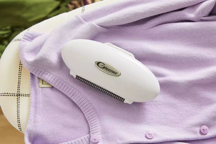 The Gleener On The Go Portable Compact Fabric Shaver & Lint Remover in use on a purple cardigan