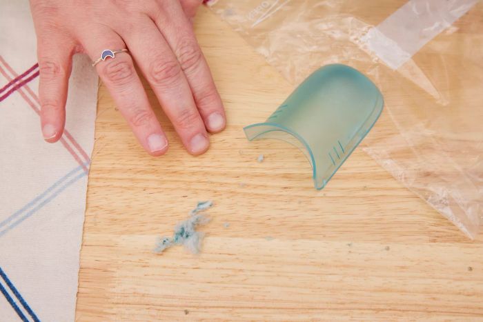A hand resting on a wooden table beside a compartment from the Philips GC026 Electric Lint Remover and Fabric Shaver, with fabric shavings nearby