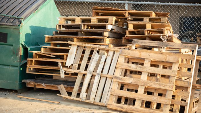 A stack of wooden shipping pallets next to a garbage dumpster