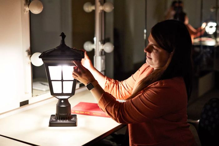 A person is seen holding the Kemeco Solar Post Light with Mount, placed on a white tabletop