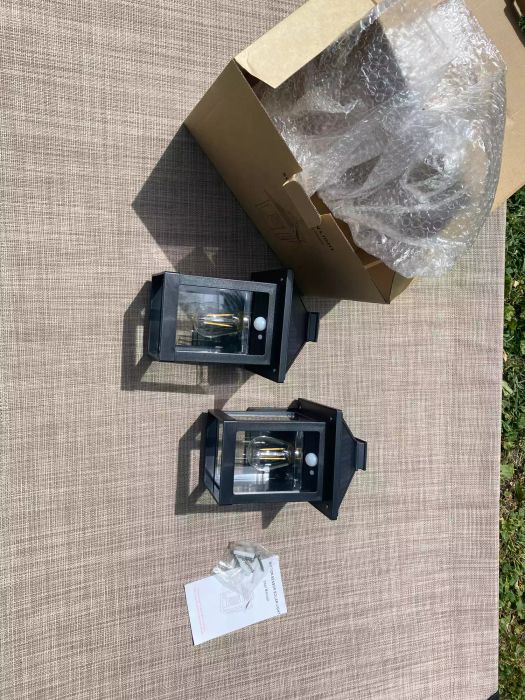 Cyhkee Solar Wall Lanterns are shown on a fabric lawn chair, accompanied by a cardboard box and bubble wrap.