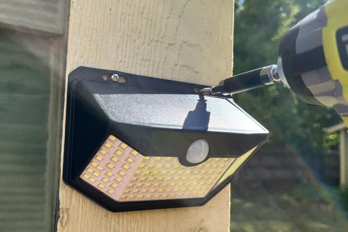 Drill fastening an HMCITY Outdoor 120 LED Solar Light to the corner of a house