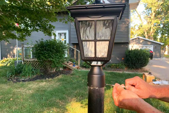 Two hands attaching the Kemeco Solar Post Light to a pole outside a house.