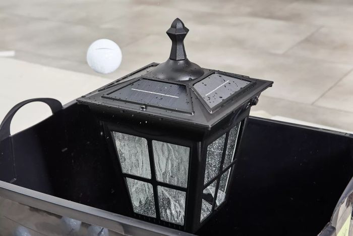 The Kemeco Solar Post Light with Mount rests inside a black basket, with a golf ball dropping onto it