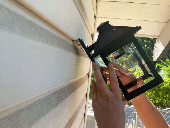 Hands installing a Cyhkee Motion Sensor Solar Powered Wall Lantern onto siding