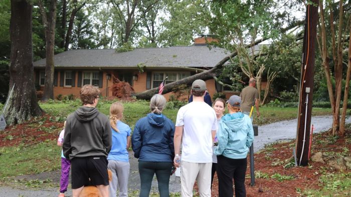 A family standing in front of their house with a tree collapsed on the roof.