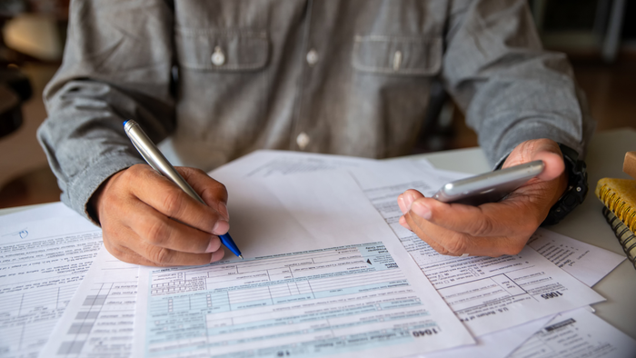 A man completing tax forms while using a calculator on his smartphone