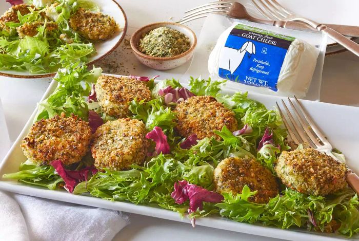 This is a shot of Trader Joe's Chevré Goat Cheese, featured in the Green Goddess Fried Goat Cheese recipe. The cheese is displayed on a rectangular platter over a bed of fresh lettuce, with a small dish of Green Goddess Seasoning Blend placed in the background.