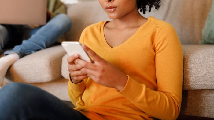 Woman texting on a phone with another person in the background