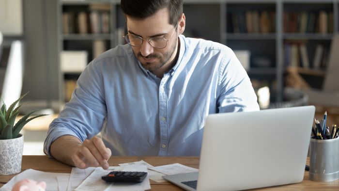 A man analyzing financial accounts on his computer while using a calculator
