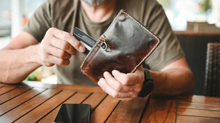 A man taking out a credit card from his wallet while seated at a café table